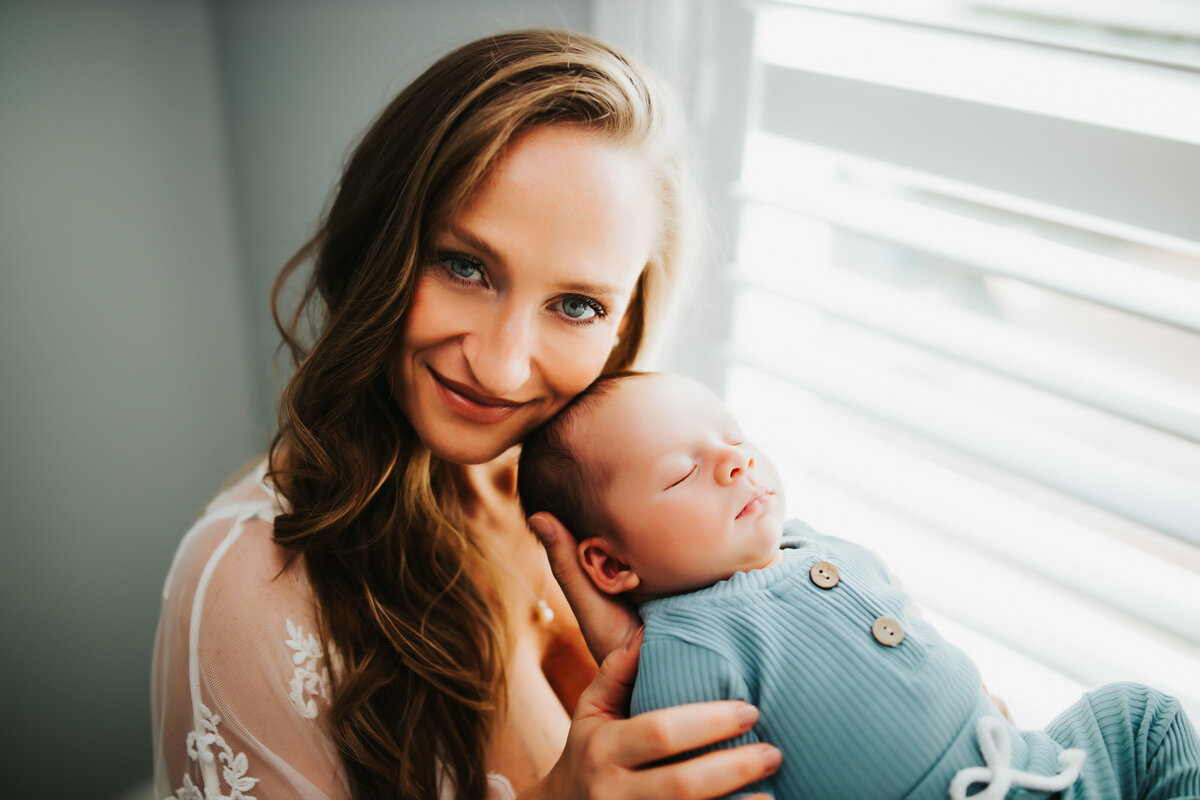 a mom cuddling her face next to her baby looking directly at the camera during a lifestyle newborn shoot