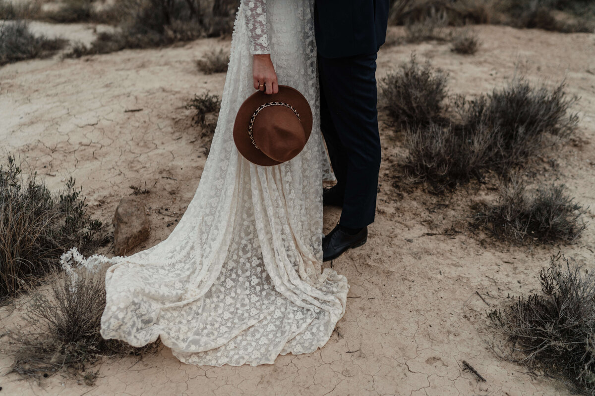 bride-holding-hat-groom-standing-near-bushes (1)