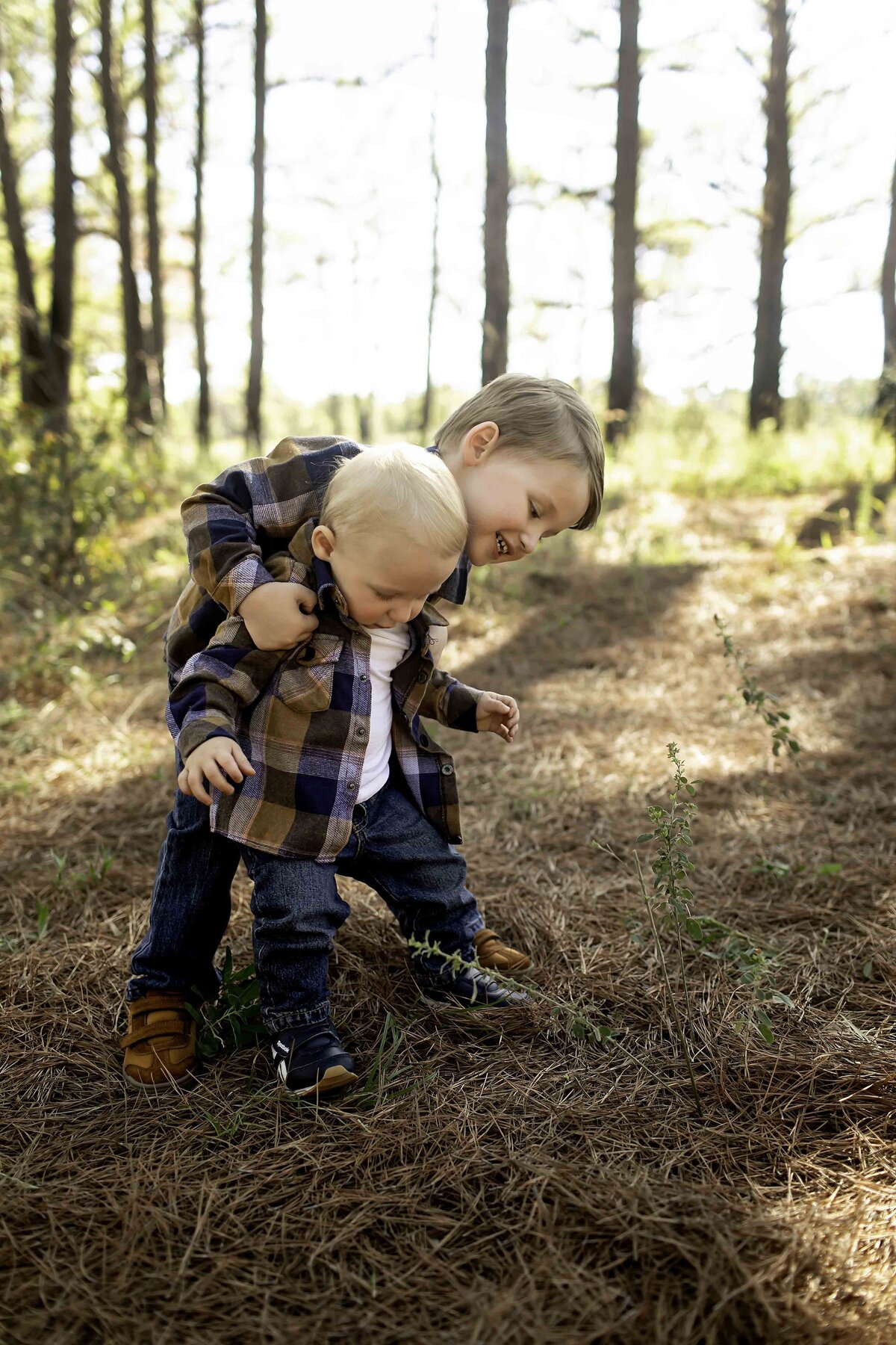 Birthday boy and big brother standing hand in hand in a pine tree forest, with big smiles on their faces