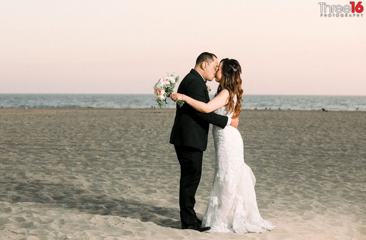 Bride and Groom share a kiss while standing on the beach