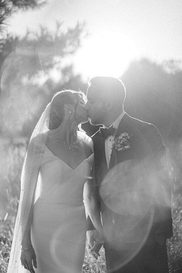 Les mariés s'embrassent sous le soleil couchant. Cette photo est douce, lumineuse et romantique.