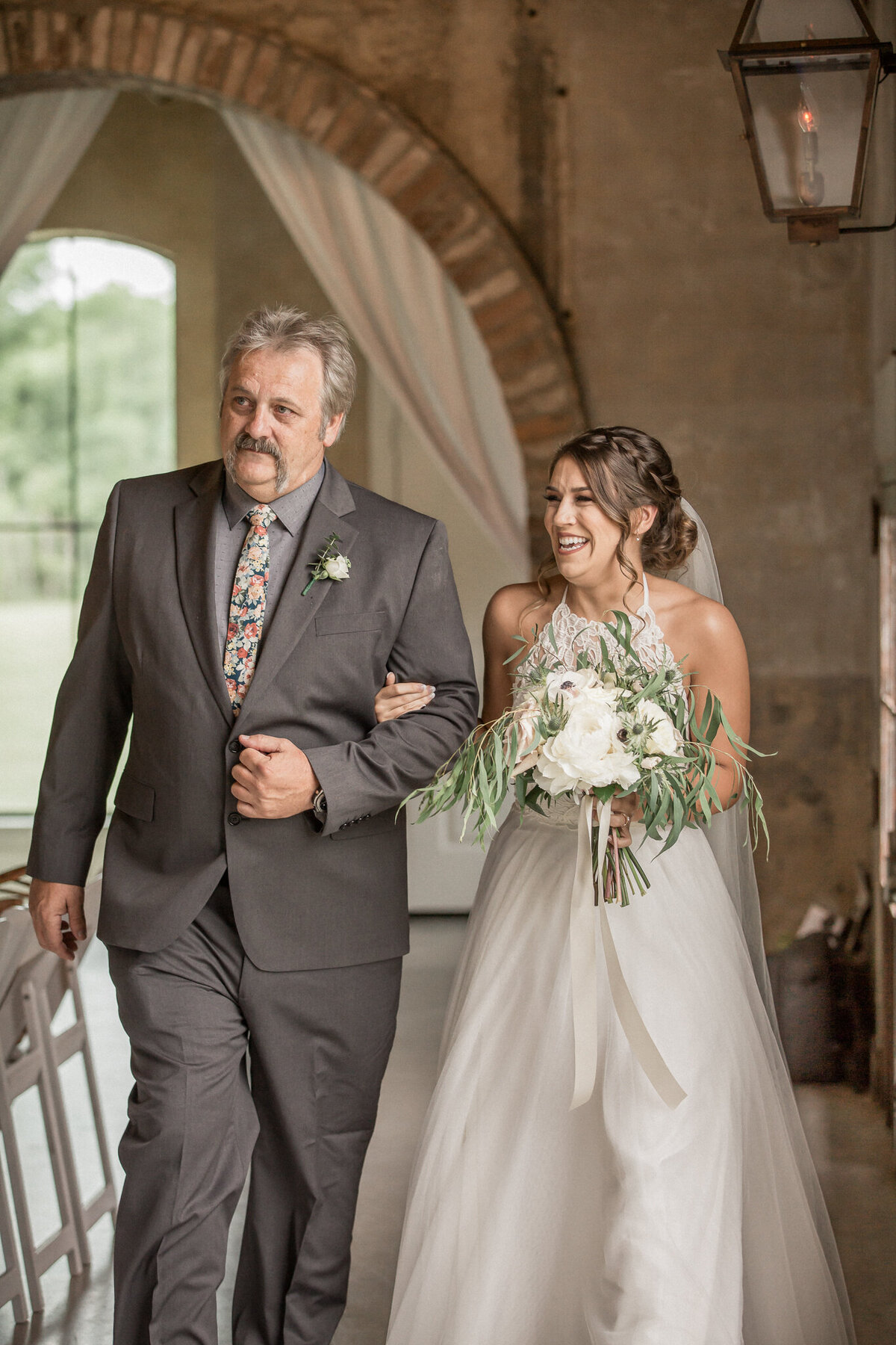 The bride, with a huge smile on her face, walks down the aisle escorted by her father