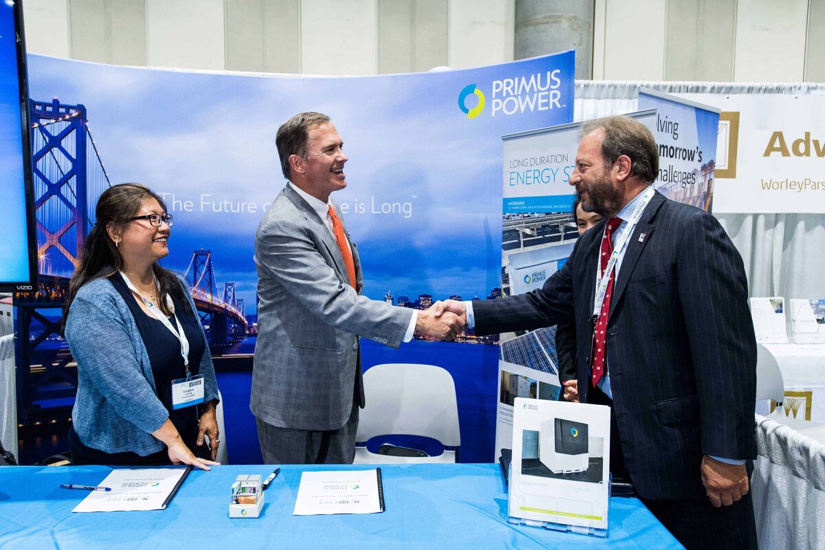two businessmen shake hands at expo booth table