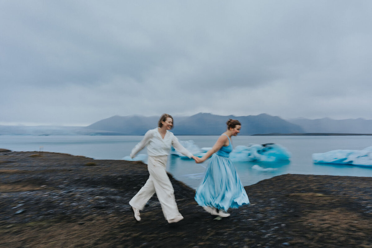 Lesbian couple runs down the Black Sand Beach smiling 