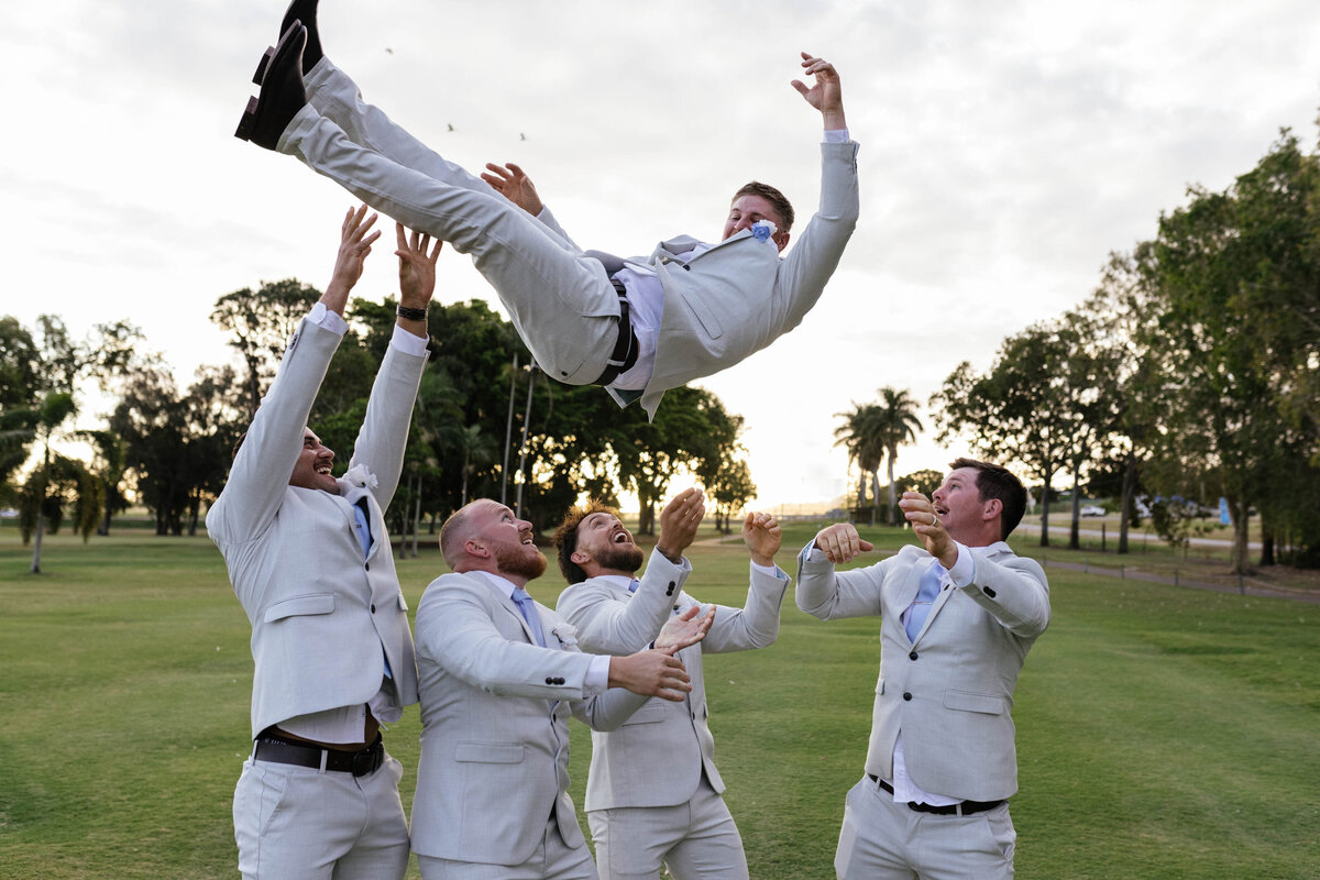 The groom is thrown into the air by his groomsmen, showing a spontaneous, fun moment. 
