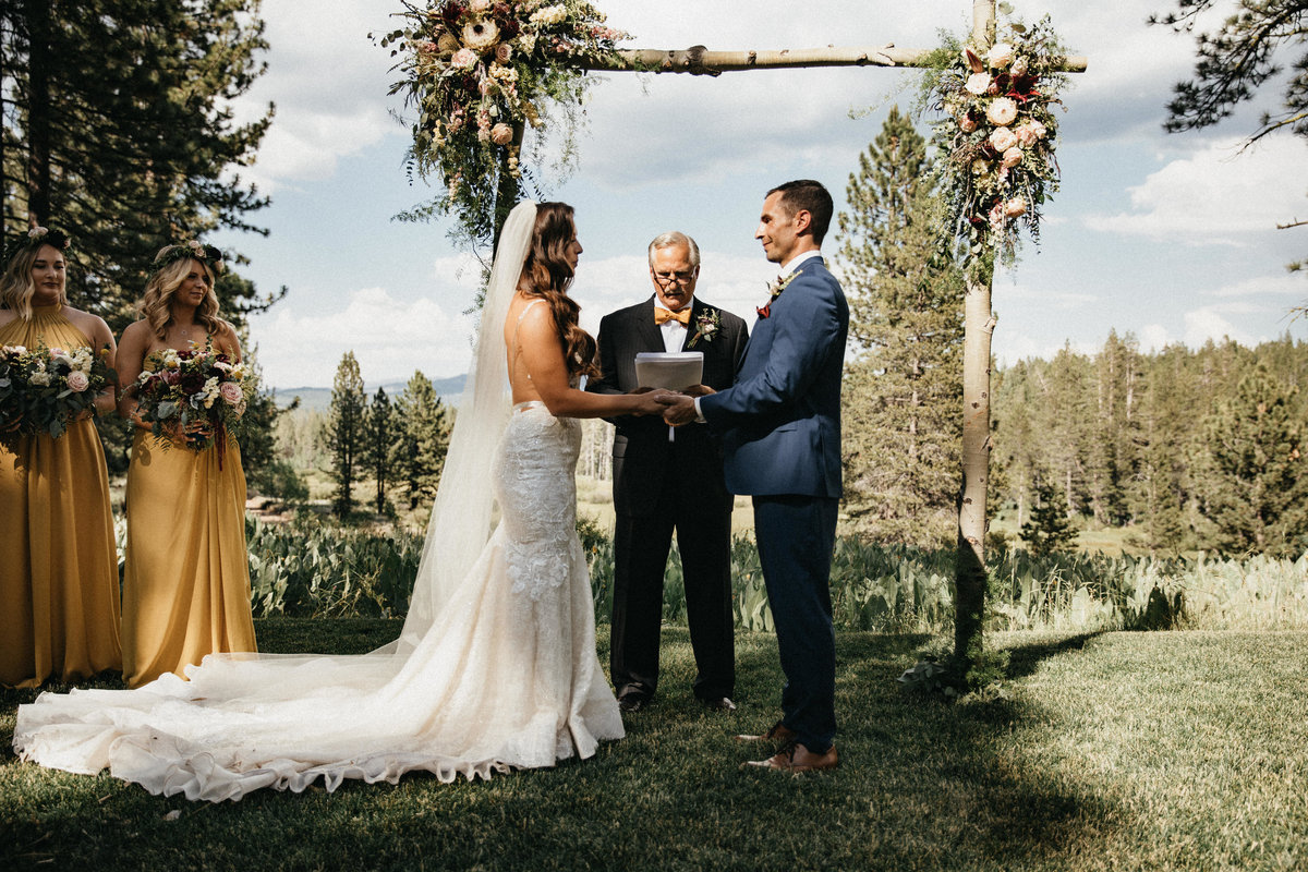 Tahoe Wedding Planners couple saying vows under floral arbor  at summer wedding venue Mitchell's Mountain Meadows Sierraville near Truckee, Joy of Life Events image by Lukas Koryn