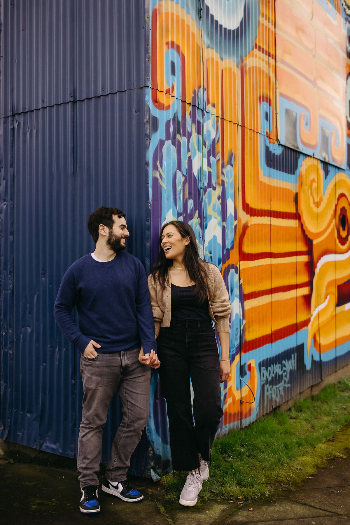 Engagement couple holds hand on blue and orange graffiti wall wall