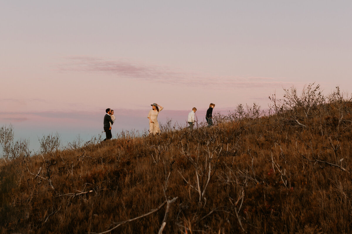 Family of five walking along a hilltop in the Blue Mountains during sunset, captured with soft pastel skies and a scenic Australian bush backdrop.