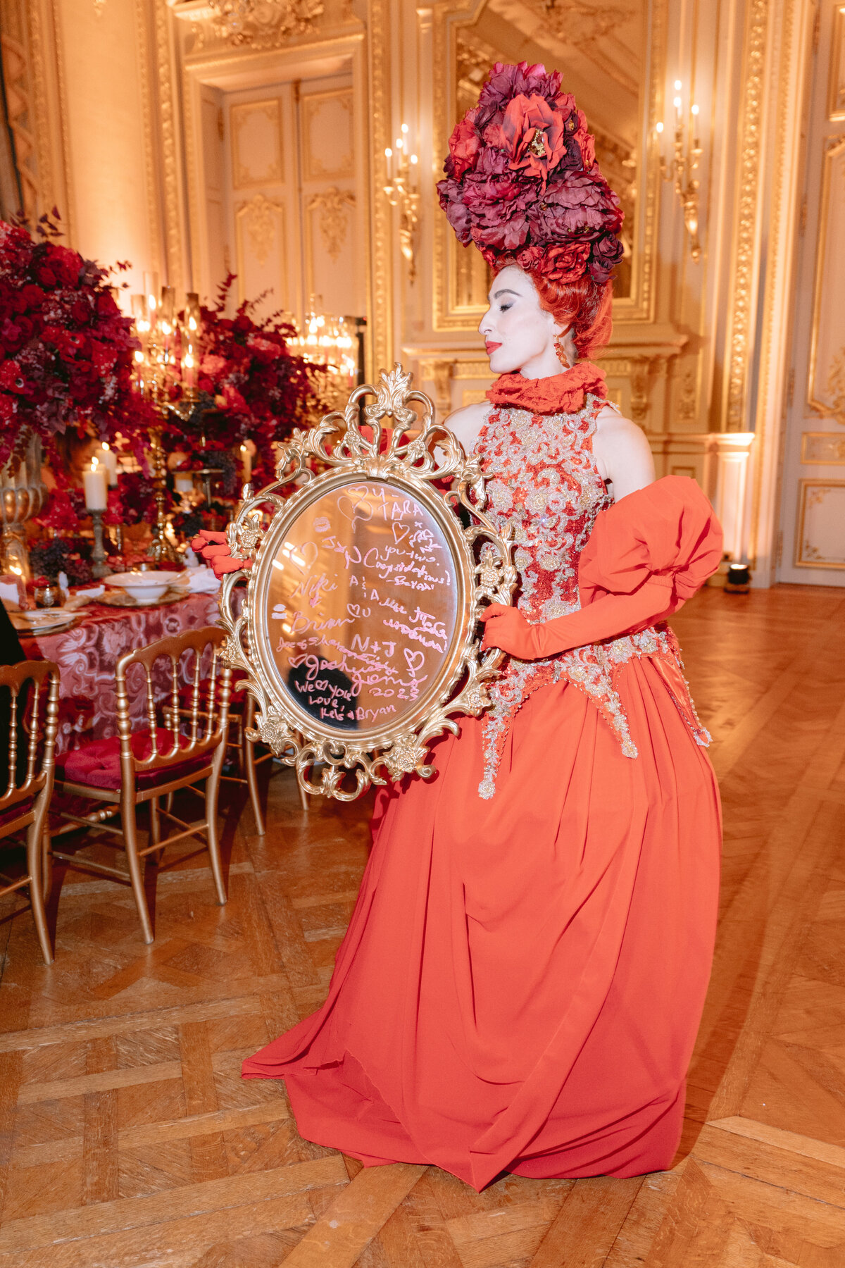 The stunning photoshoot was brought to life by the brilliant videographers at Zen Film Works, who skillfully captured the essence and magic of the luxurious Shangri La Hotel & Ritz Paris Hotel in Paris, France. Renowned for their elegance and grandeur, these locations provided the perfect backdrop for the mesmerizing shot.  The talented photographer, Matteo Coltro, with his exceptional eye for detail and artistry, beautifully captured the captivating person adorned in the elaborate red gown and intricate gold embroidery. The large floral headpiece added a touch of exquisiteness to the scene, perfectly complementing the overall aesthetic.  With the ornate, oval-shaped mirror adorned with handwritten messages, the subject exuded a sense of mystique and sophistication, making the composition truly captivating. The opulent room, filled with lavish gold accents, striking red floral arrangements, and exquisite ornate furniture, enhanced the beauty and allure of the overall setting captured by Zen Film Works and Matteo Coltro.