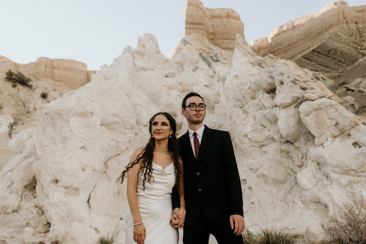 portrait of a bride and groom standing together in front of a massive white rock in New Mexico