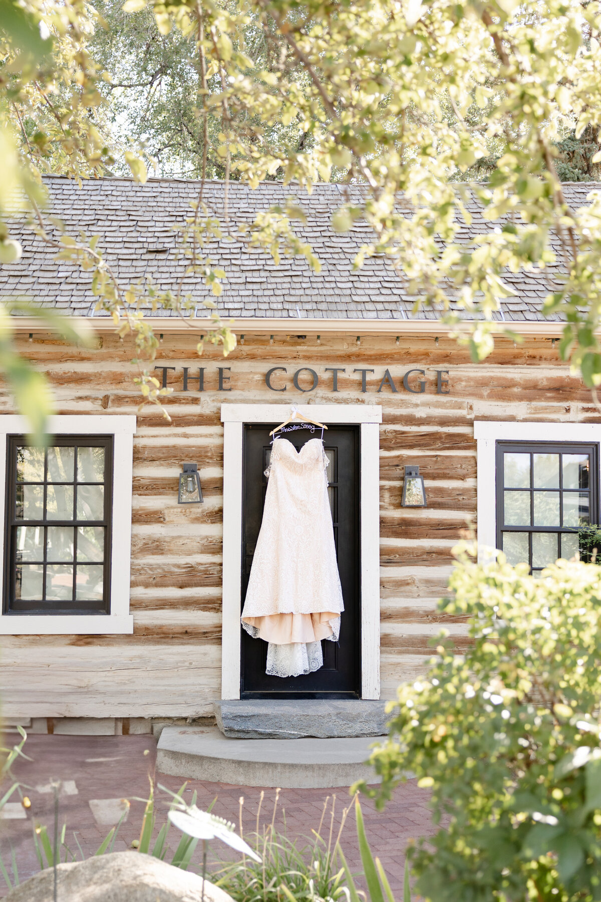 Wedding dress hangs from door of The Cottage and is beautifully framed by greenery