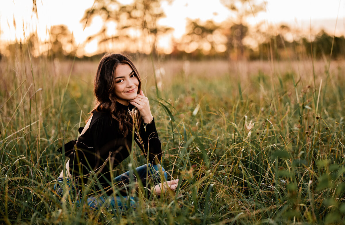 A Houston senior sits in a field of long grass at sunset.