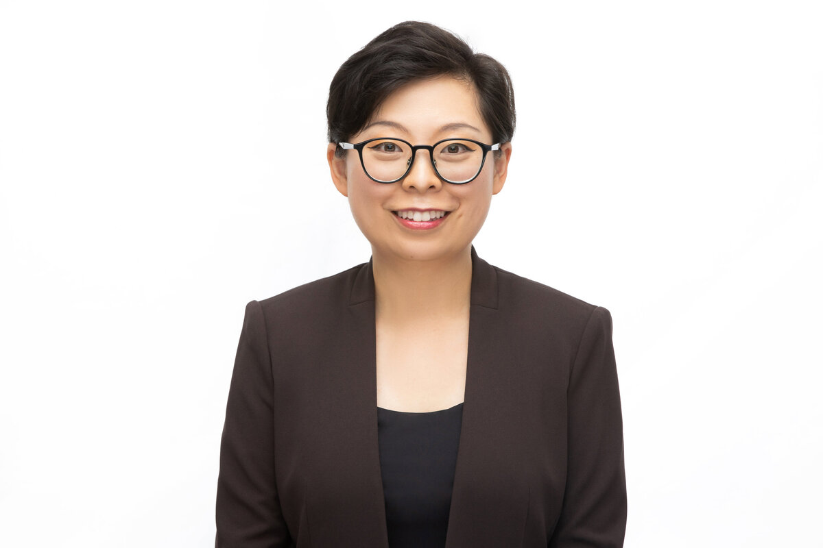 An Asian American woman female professional doctor medical researcher with glasses in a brown blazer poses for a professional headshot on a white background for Janel Lee Photography studios in Cincinnati Ohio
