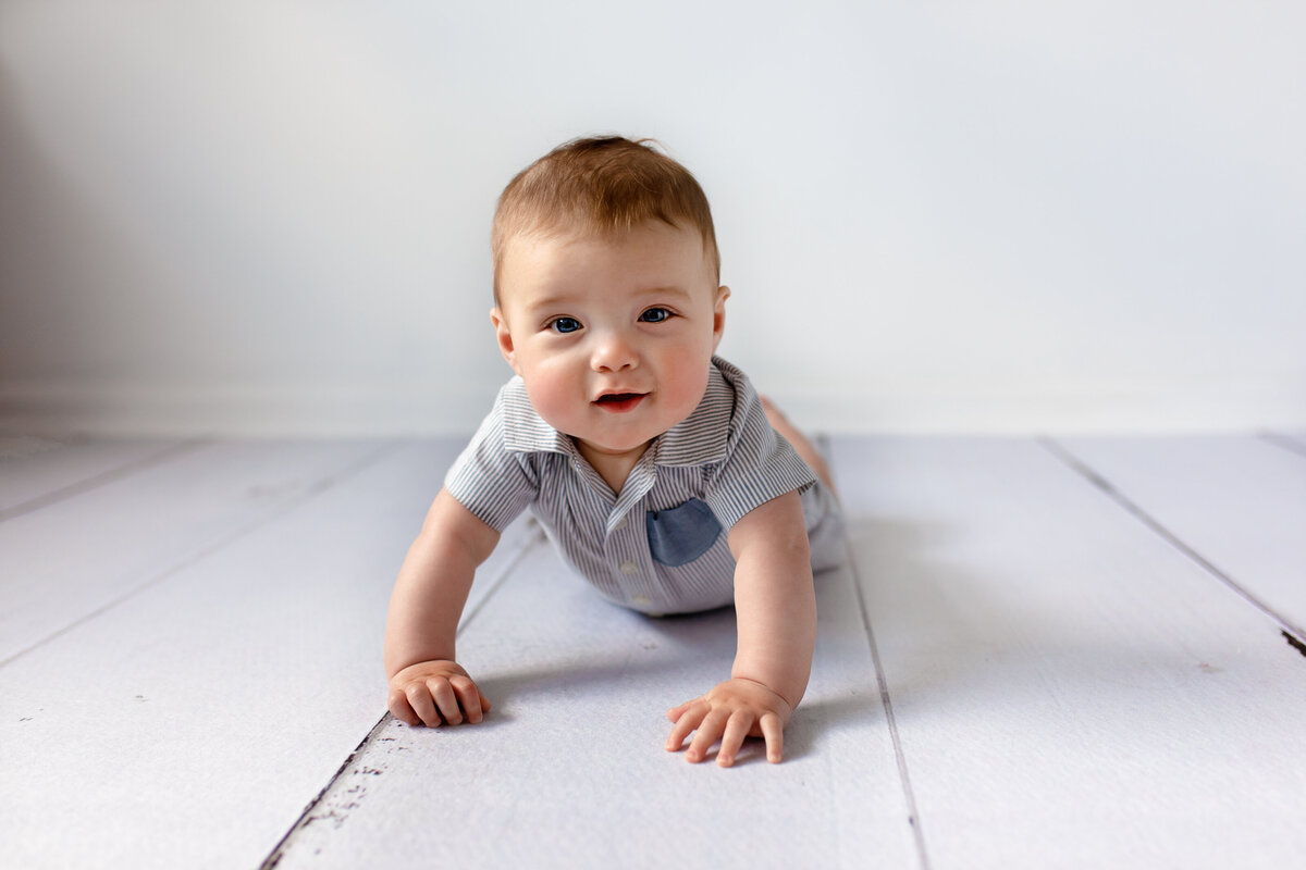 6 month baby boy laying on white wood plank floor in studio