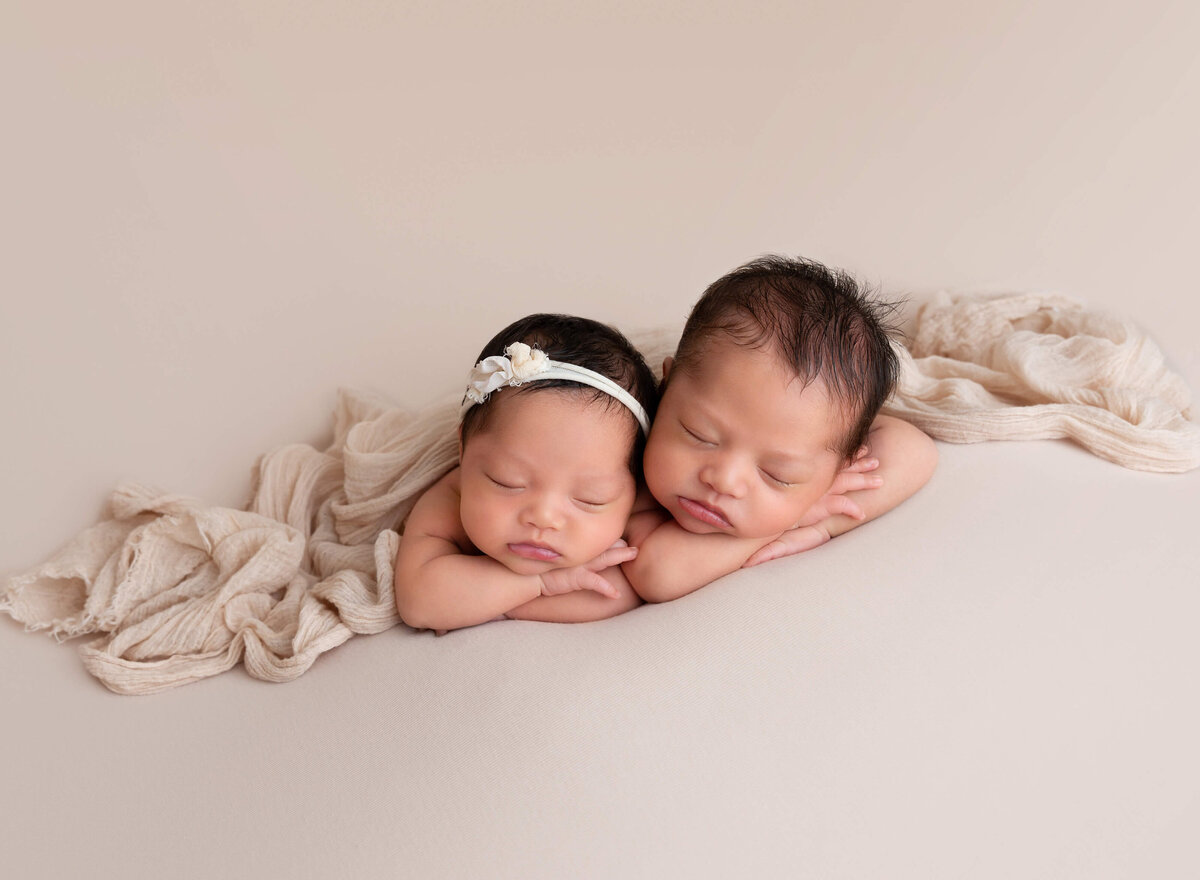 Top Brooklyn, NY Newborn Photographer captures twin boy and girl are lying on their bellies sleeping. Babies arms are folded under their chin. Babies heads are resting together.
