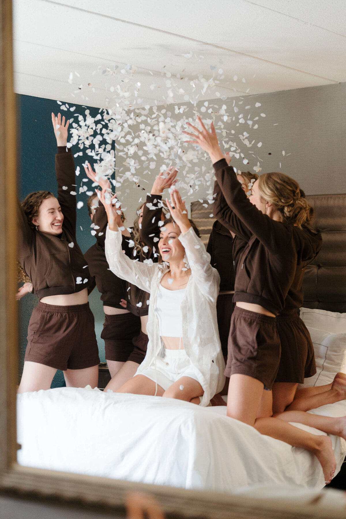 Bridesmaids joyfully throw colorful confetti onto a beautifully made bed, celebrating a special occasion together.