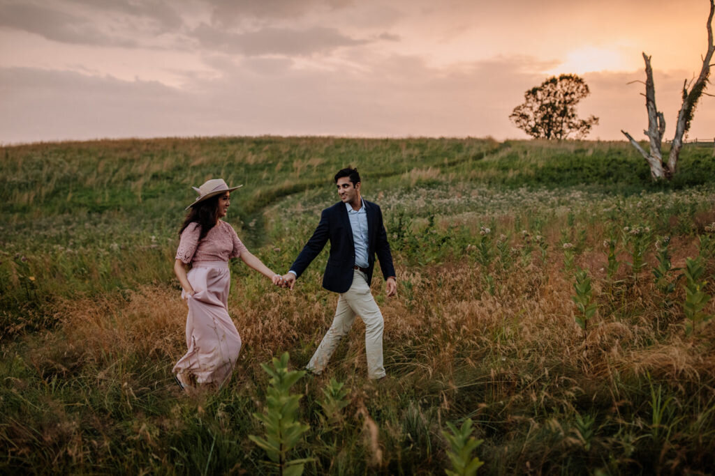 Bride and groom holding hands looking at each other while standing in front of rolling hills with the sunlight coming down on them