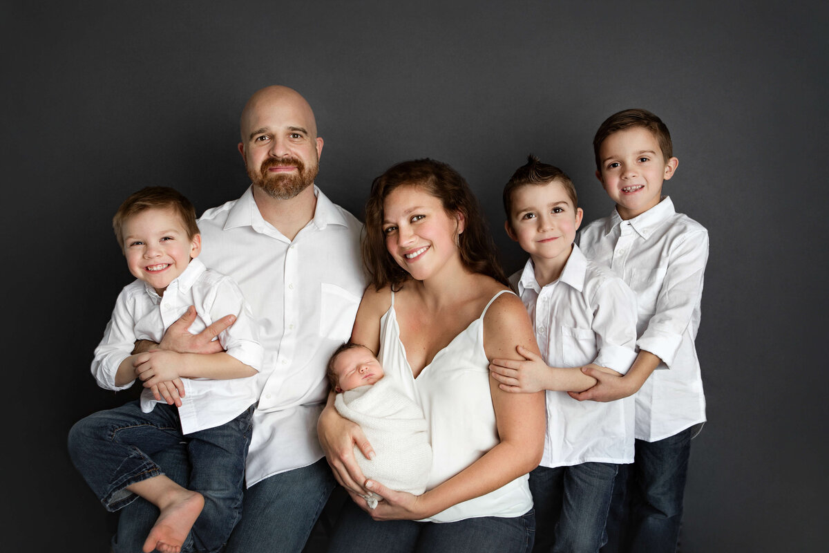 family photo- mom, dad, 3 young brothers,  and newborn  baby  boy- in jeans white shirts on a grey backdrop