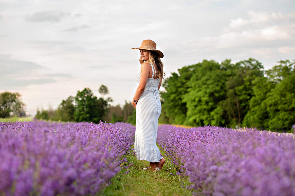 pregnant woman wearing a blue and white dress with her back to the camera in the Toronto lavender field.