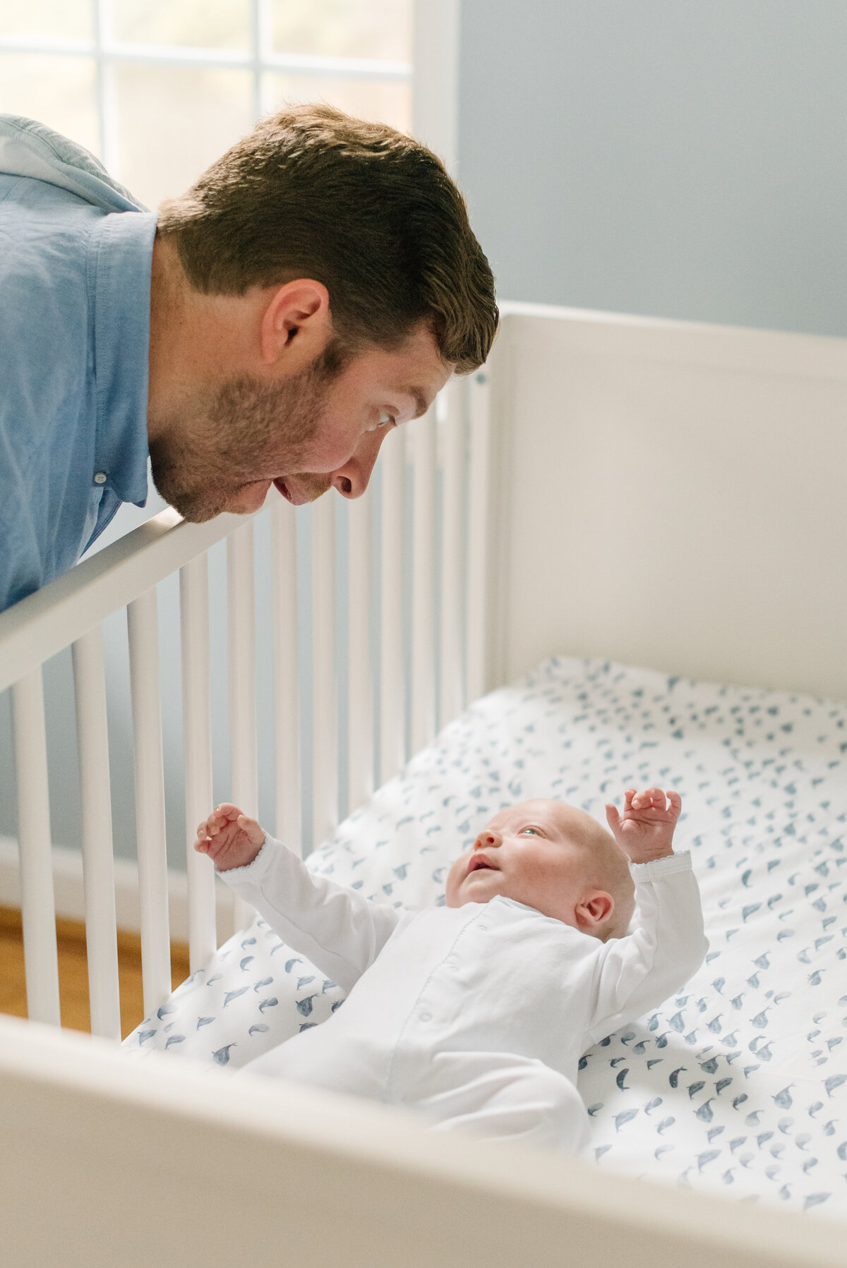 Father making funny faces at his baby in a white crib