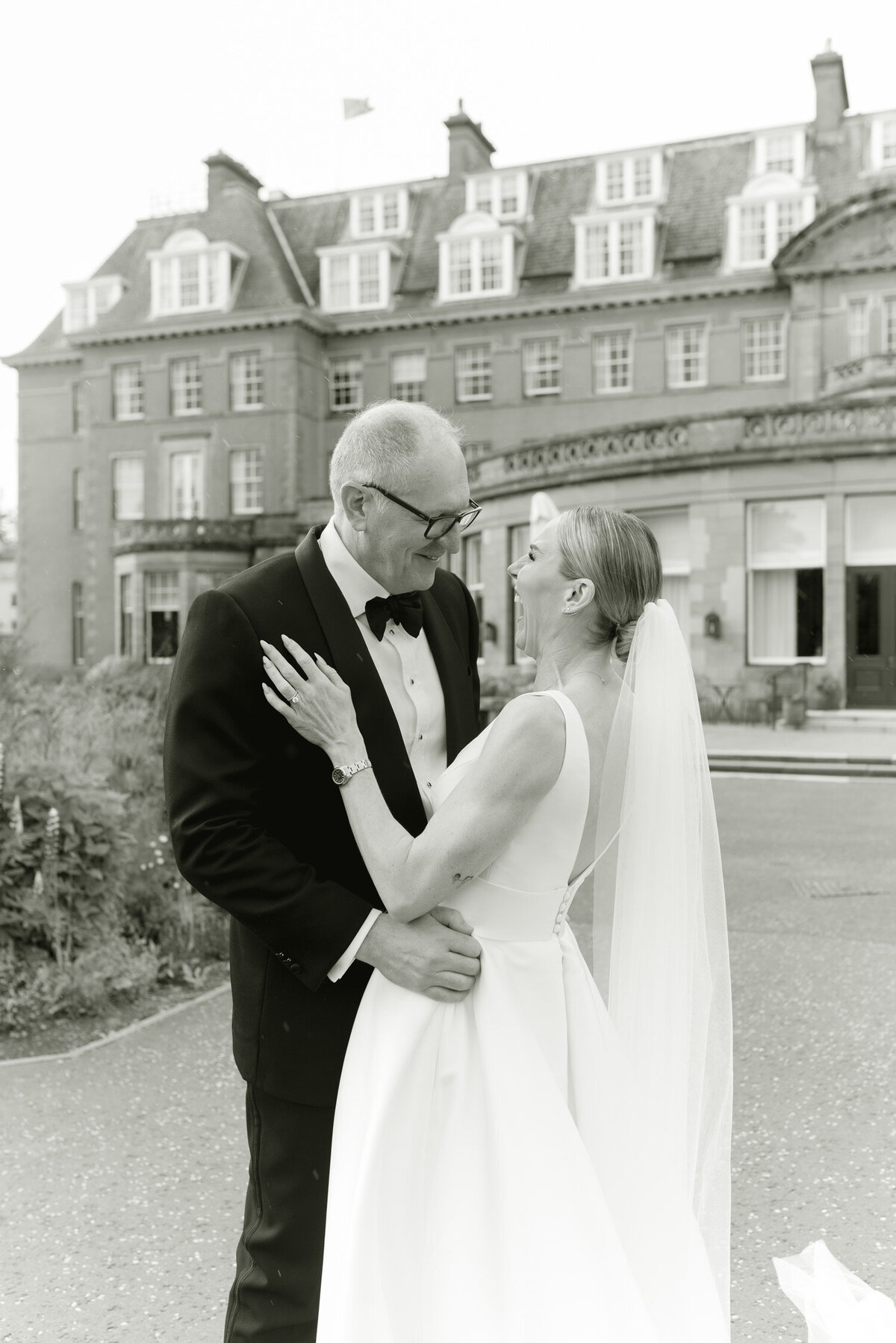Brida and Groom laugh and embrace on their wedding day at Gleneagles Hotel Scotland. Image by luxury wedding photographer Scotland, Jill Cherry Porter.