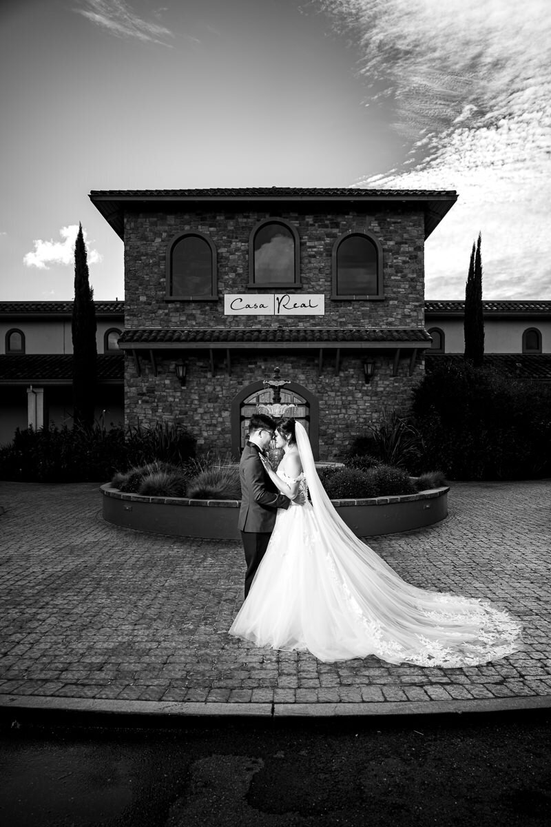 The bride and groom share a romantic and tender embrace in front of the stunning entrance of Casa Real, a timeless moment filled with love and connection on their wedding day.