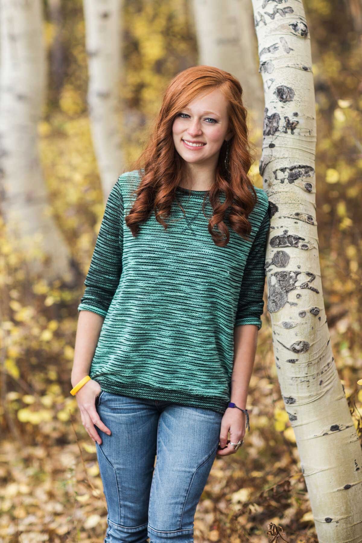 Red head girl posing in aspen trees for senior pictures in Utah canyon.