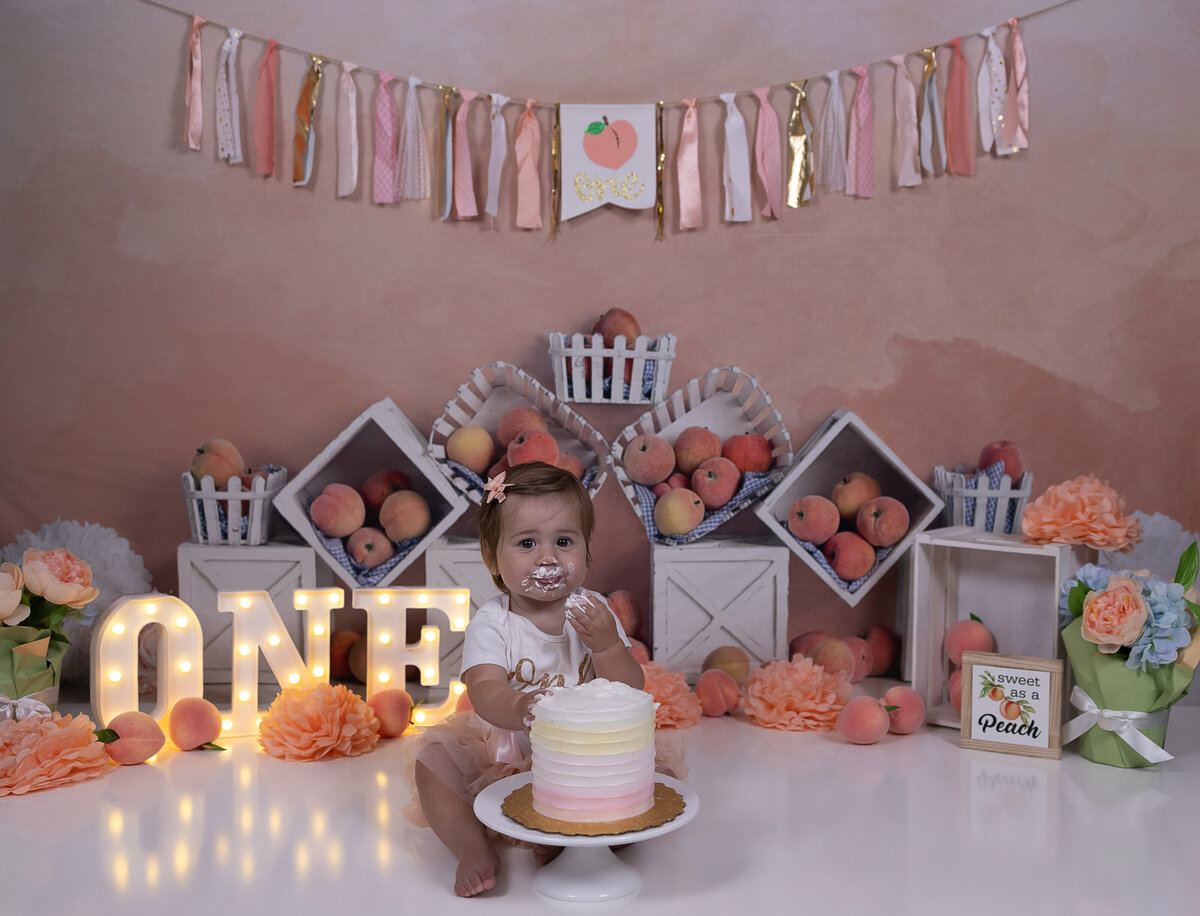 One sweet peach cake smash with peach colored pastel decorations – First birthday photo session in Bergen County NJ photography studio.