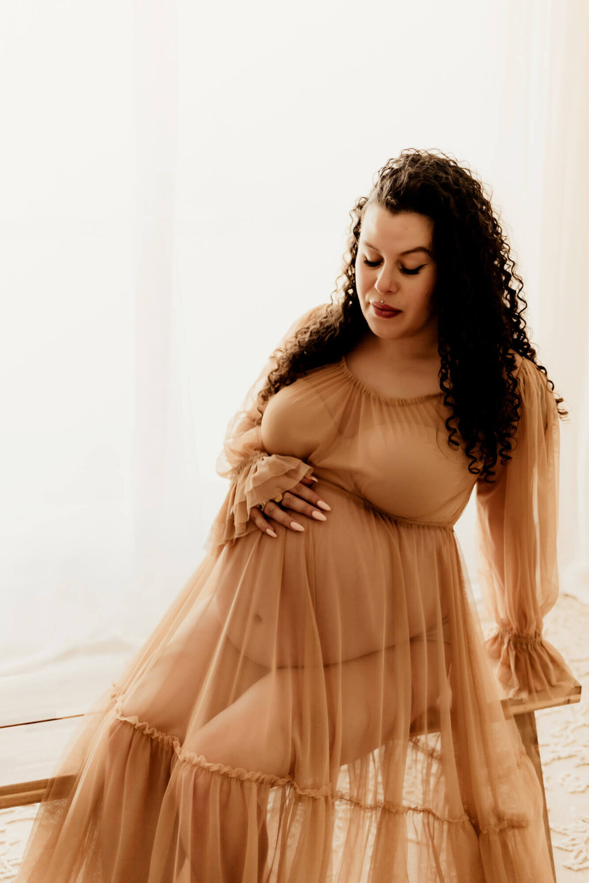 Oklahoma pregnant mother wearing a sheer tan dress and looking at her belly.