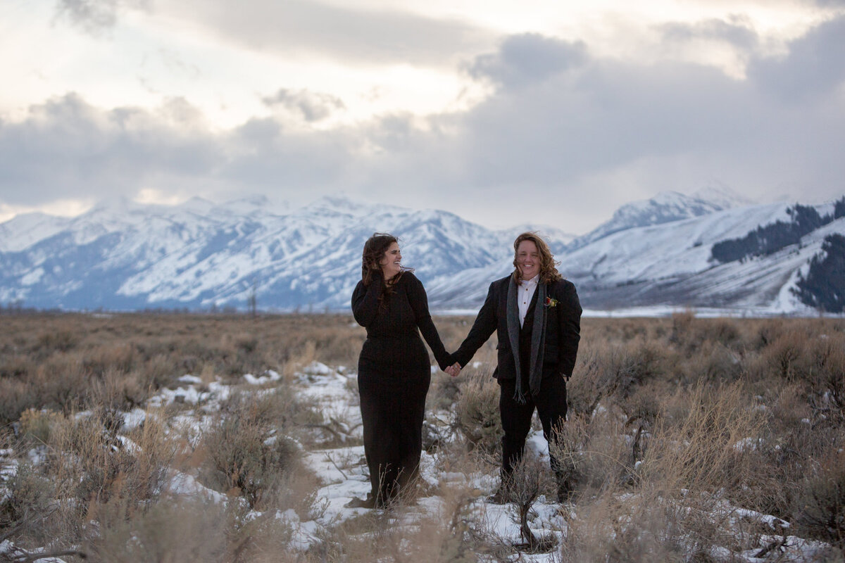 Two brides wearing black stand in a meadow on their Wyoming elopement day.