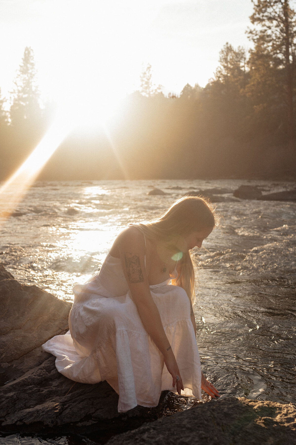woman in white dress sits next to the river and observes her surroundings as the light shines upon her