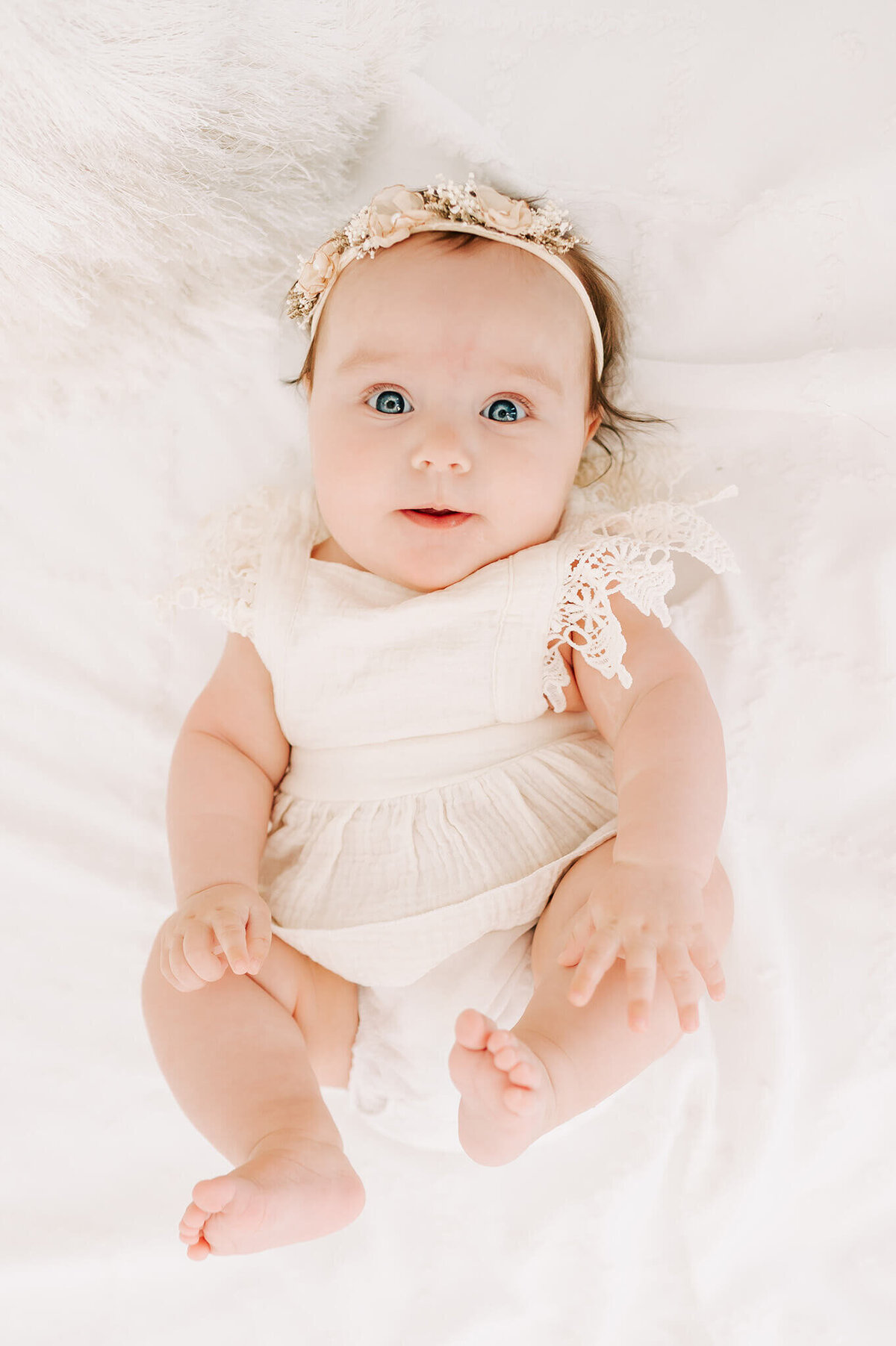 Branson family photography of baby girl in white laying on bed