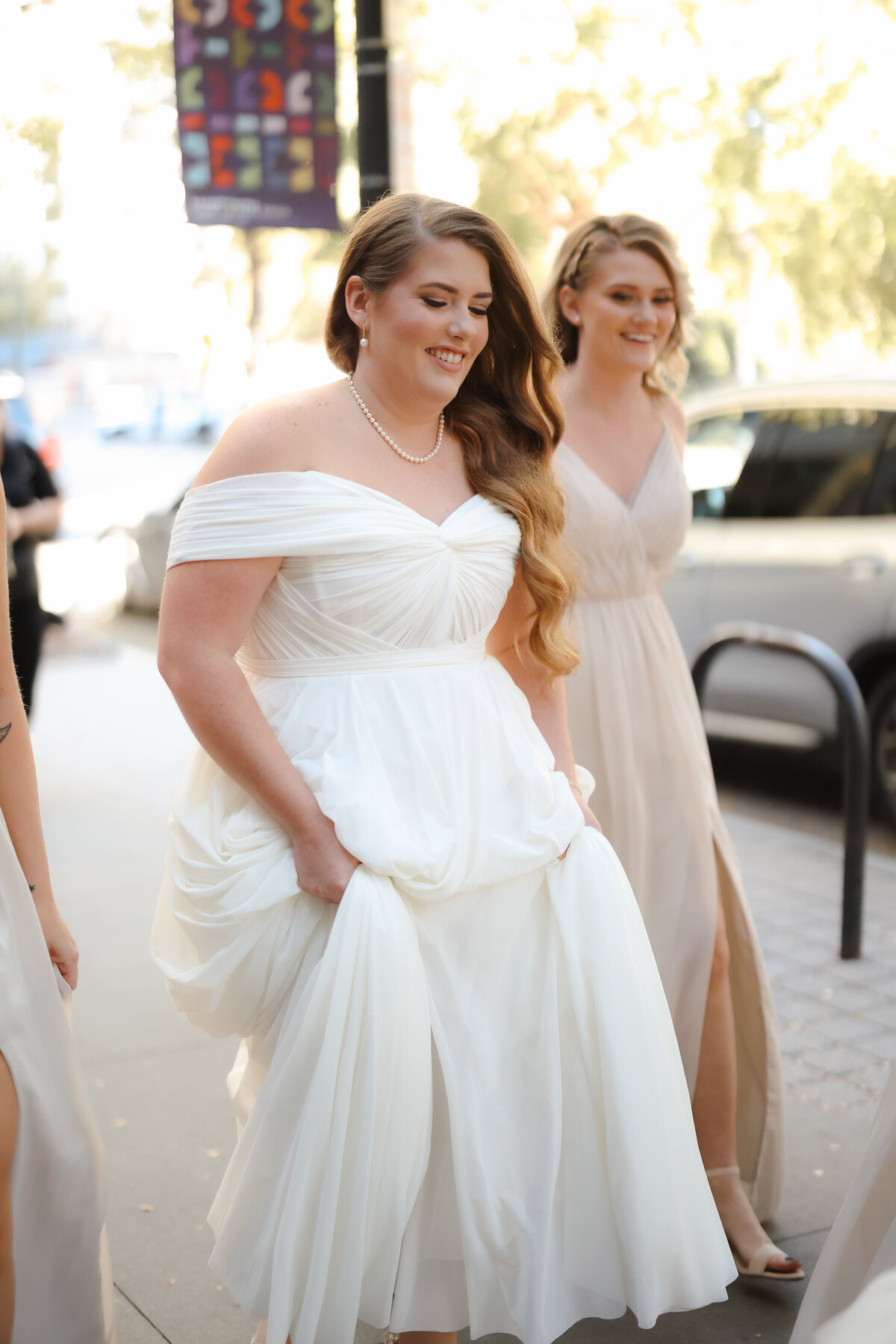 Bride surrounded by her bridesmaids as they help her get ready for the wedding, sharing laughs and joyful moments in a softly lit room.