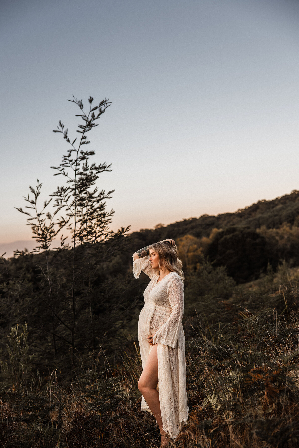 Pregnant woman stand on hillside at sunset