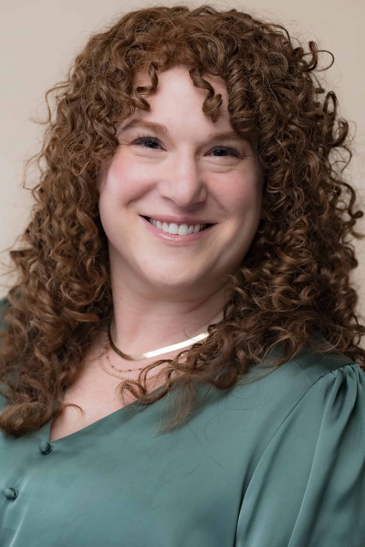 Close up headshot of a woman with long curly red hair posing for a corporate headshot