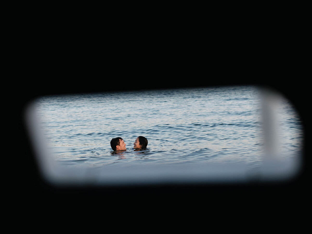 Two people are swimming in the ocean, viewed through a blurry, rectangular foreground