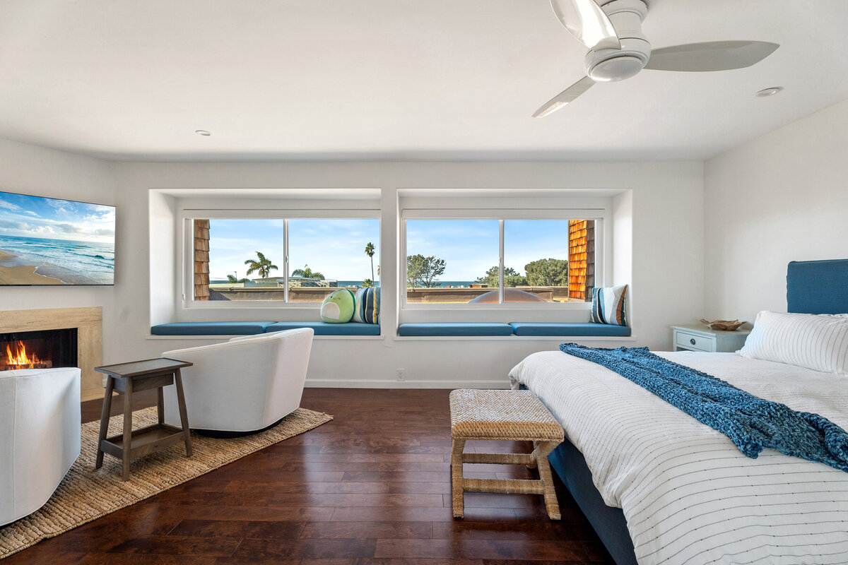 Bright white primary bedroom on the second story overlooking the ocean. Bed on the right side with a seating area on the left.