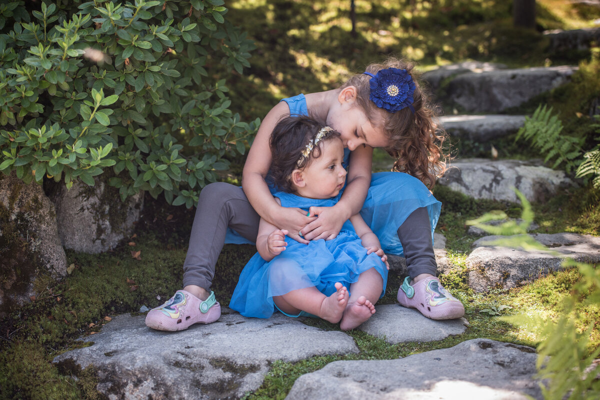 A child sitting on a stone step with their baby sibling sitting in between their legs