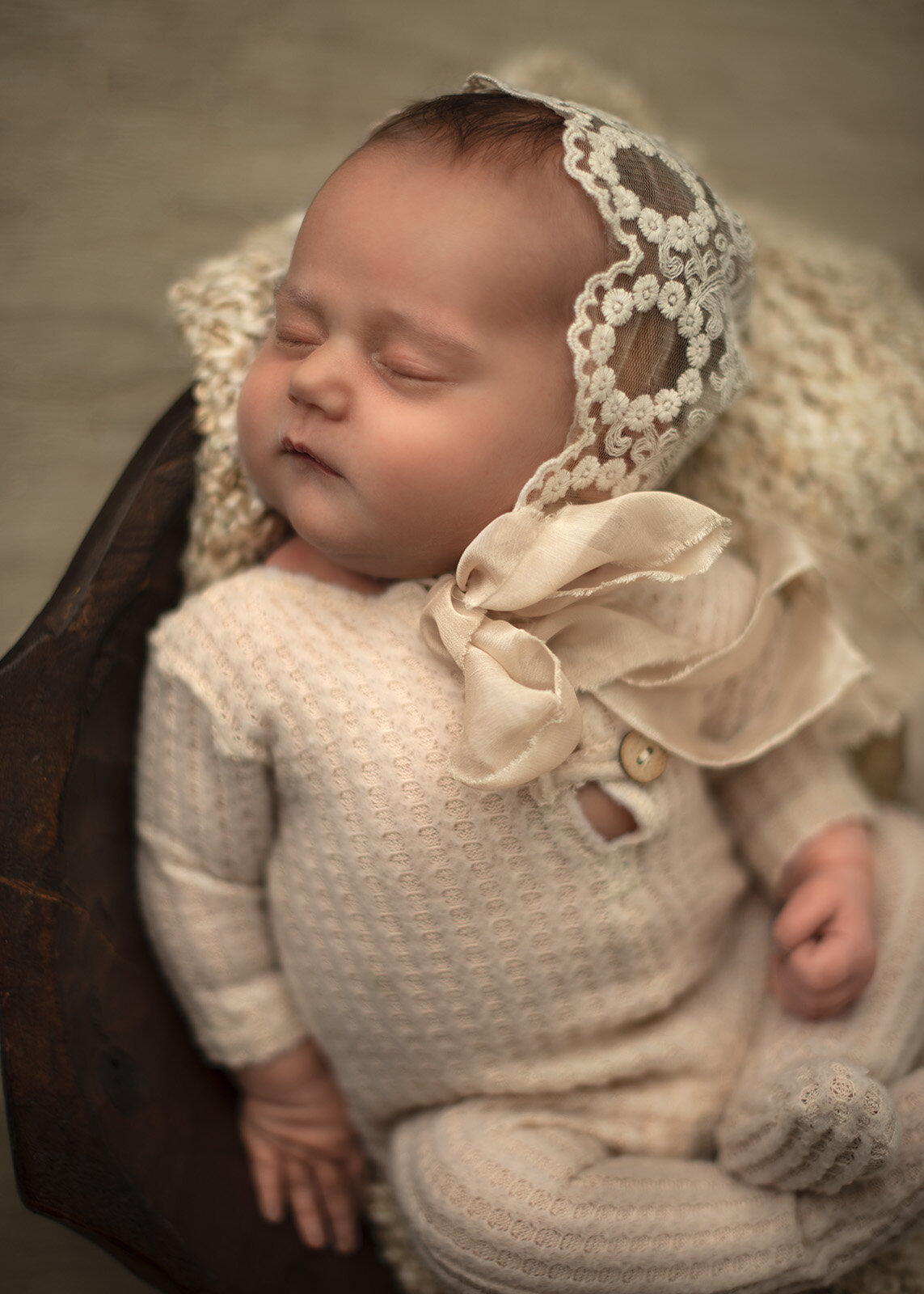 newborn in a sleeper and bonnet in a bowl at her st. louis newborn photoshoot