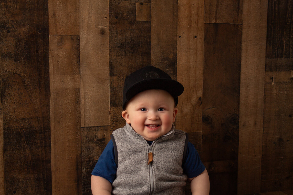 Milestone portrait of a little boy smiling with a wooden background.