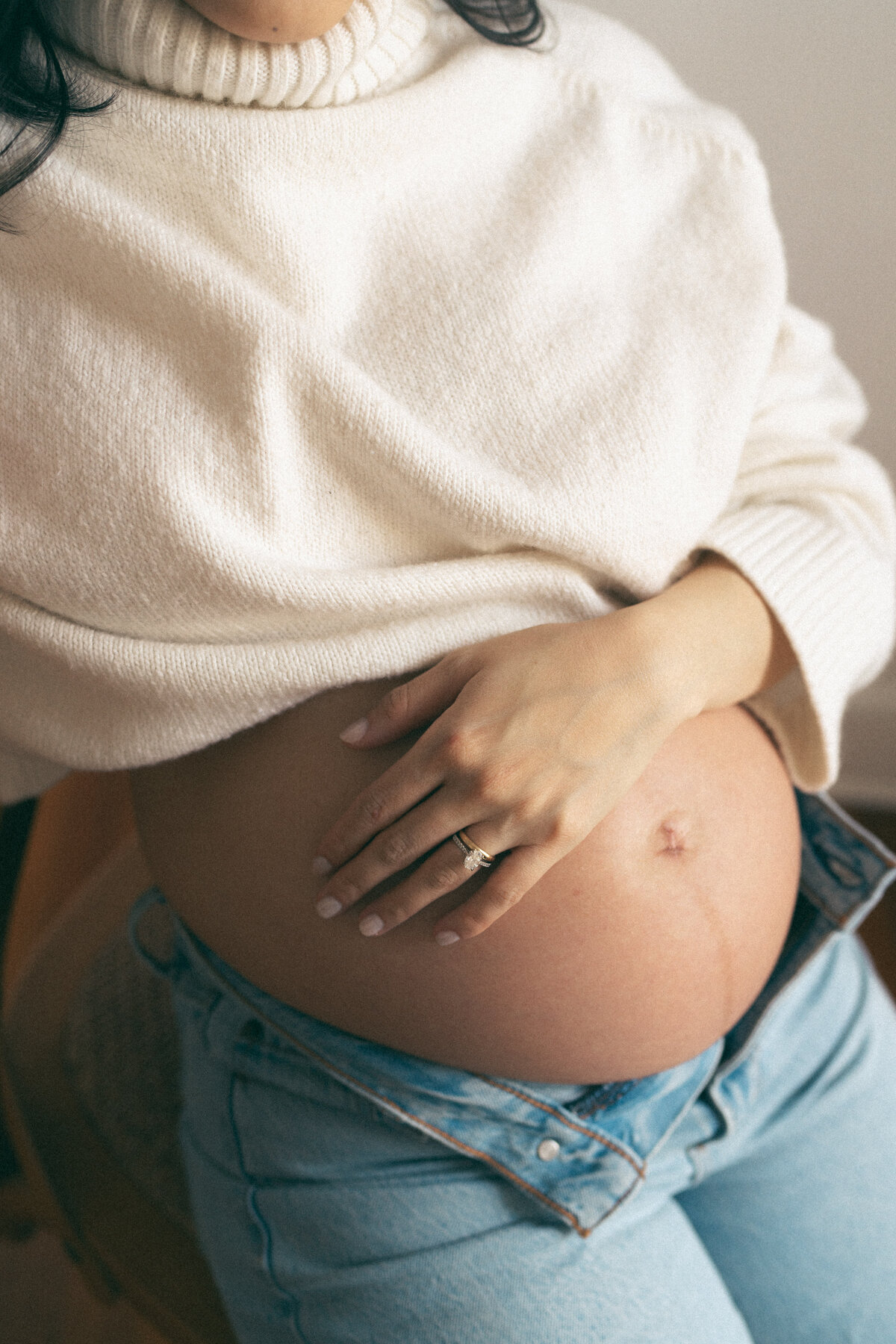 close up of a pregnant woman's hand on her belly, wearing a cozy cream sweater. 