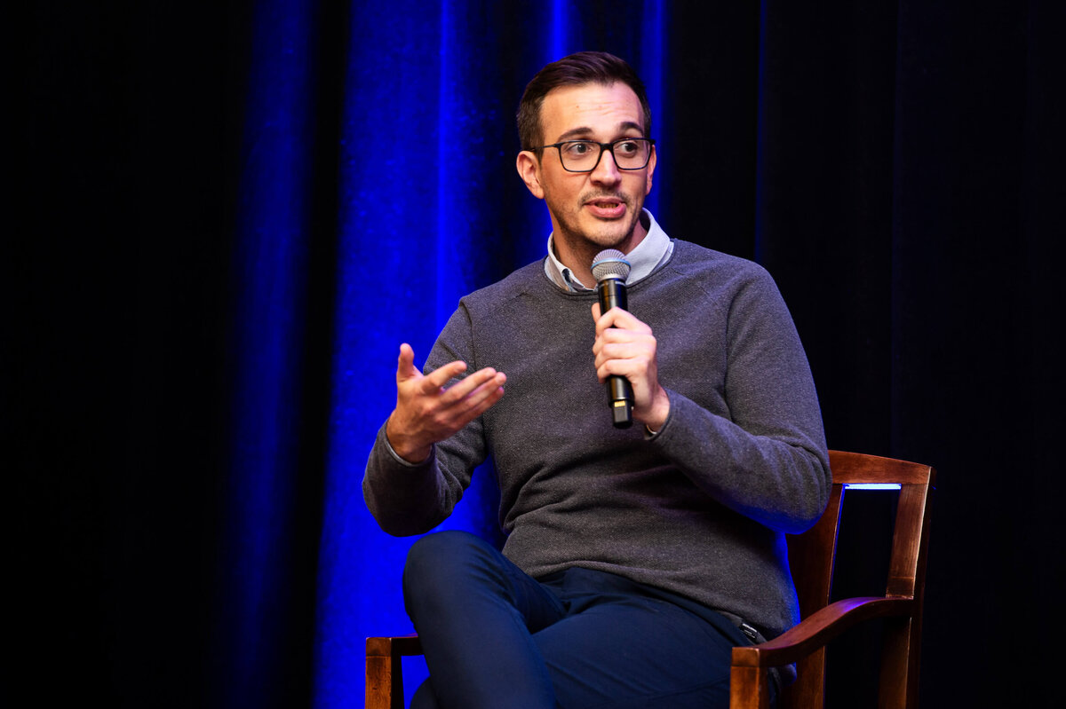 a man in a grey sweater seated and talking into a microphone during a 2-day corporate conference at the Westin Hotel.  Captured by Ottawa Event Photographer JEMMAN Photography COMMERCIAL