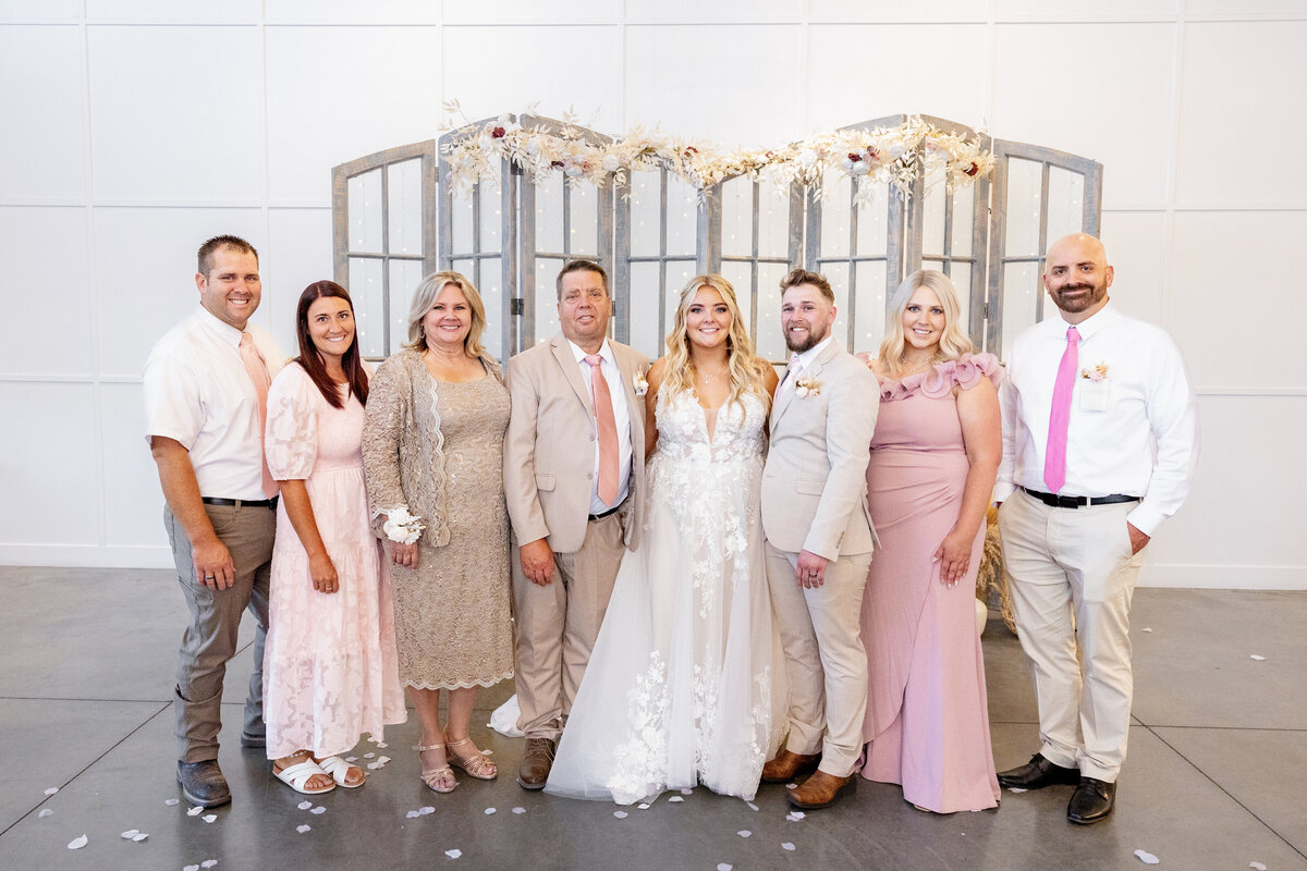 The bride and groom pose with their closest family members after the ceremony. Everyone is dressed in soft, elegant shades of blush, champagne, and beige, creating a harmonious and timeless wedding look.