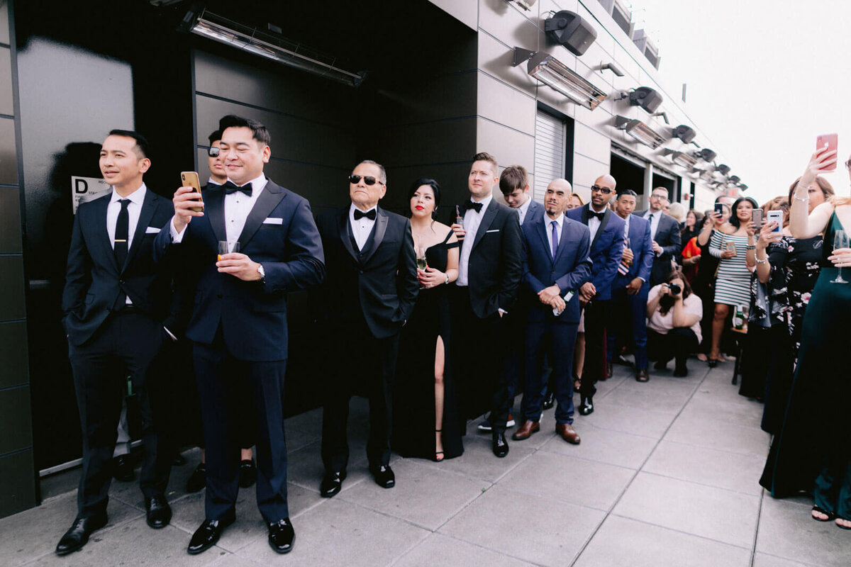 The groomsmen are lined up, taking photos using their phones in The Skylark, New York. Wedding Image by Jenny Fu Studio