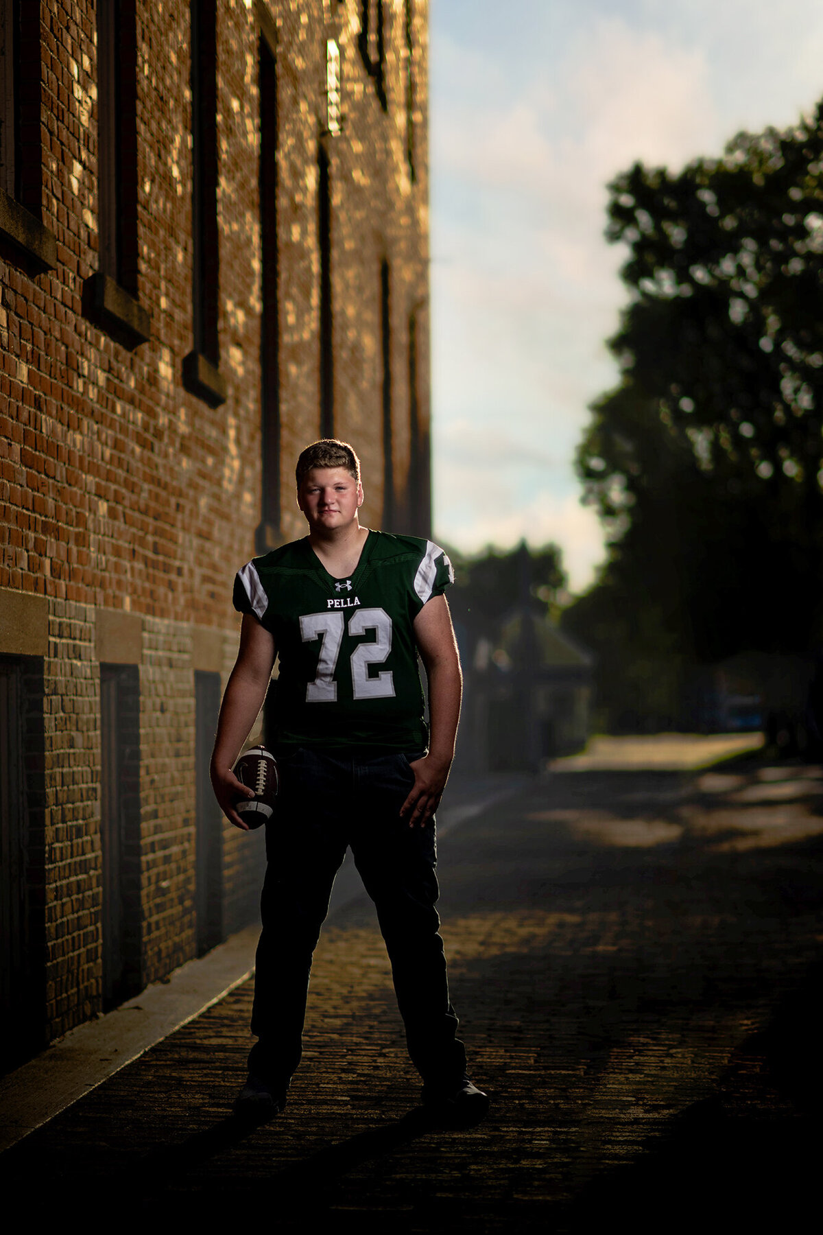 An image from a Pella Senior Photographer of a high school football player standing on a brick road