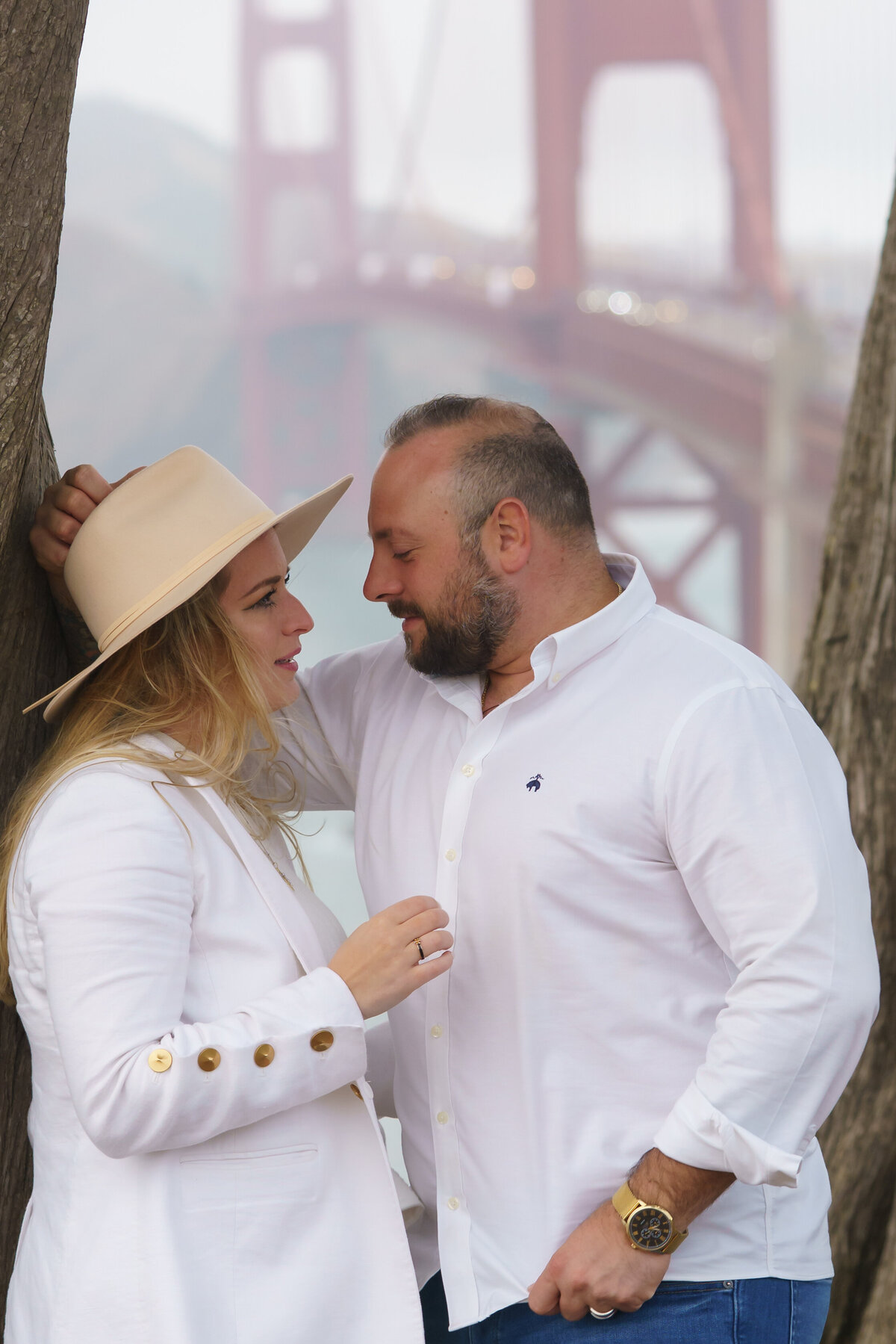 Romantic couple looking at each other while leaning against a tree in front of the golden gate bridge