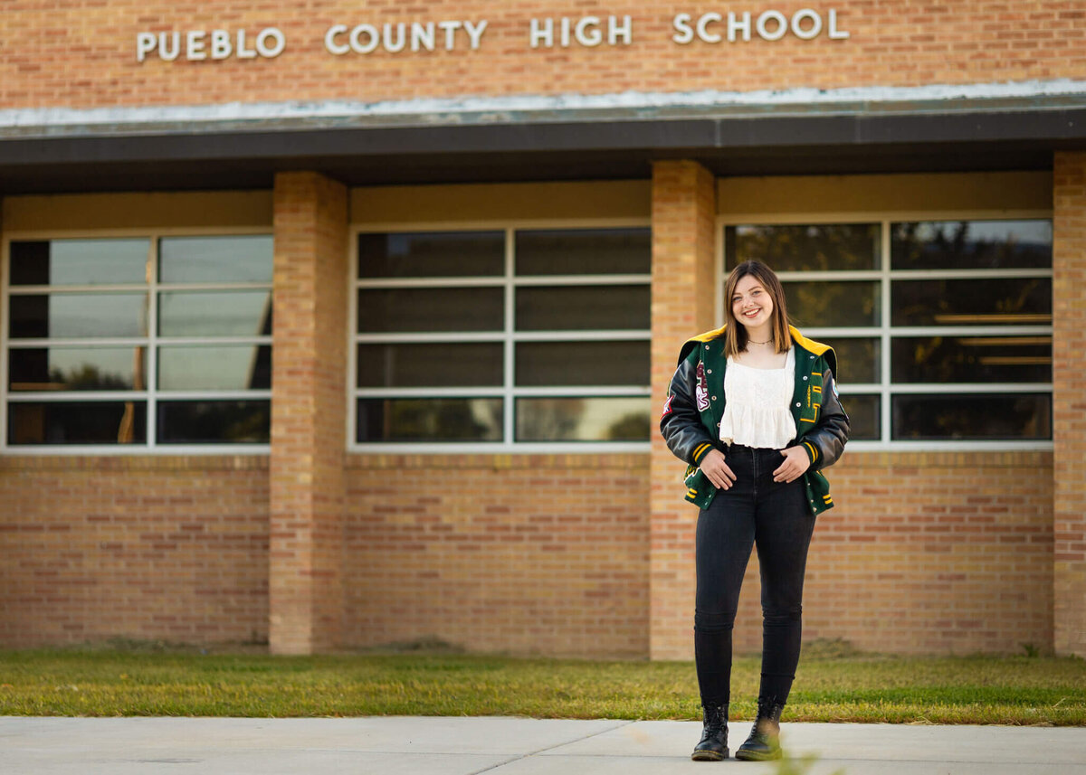 high school senior girl wearing her letterman jacket standing in front of her high school