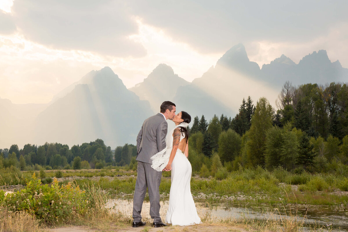A black and white wedding portrait of a couple eloping in Grand Teton National Park, with dramatic sun rays streaming through the mountains in the background.
