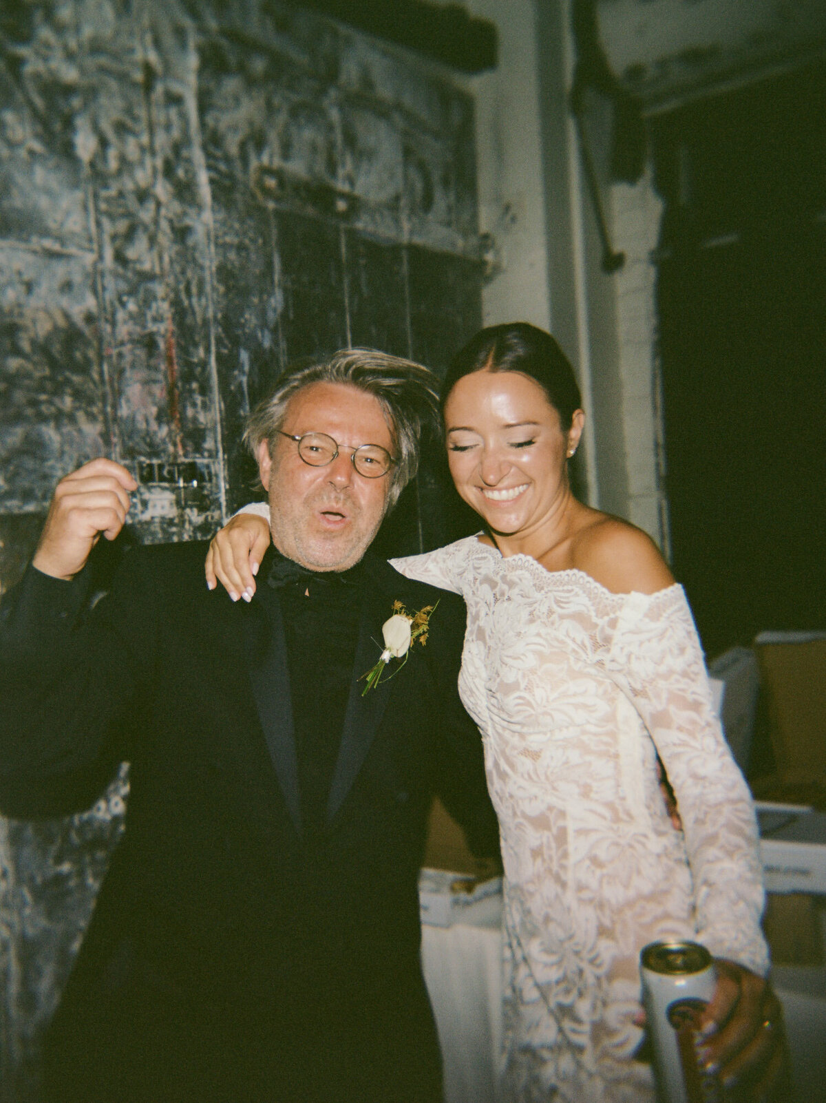 a bride in a lace afterparty dress laughs with her dad, natural film wedding photo
