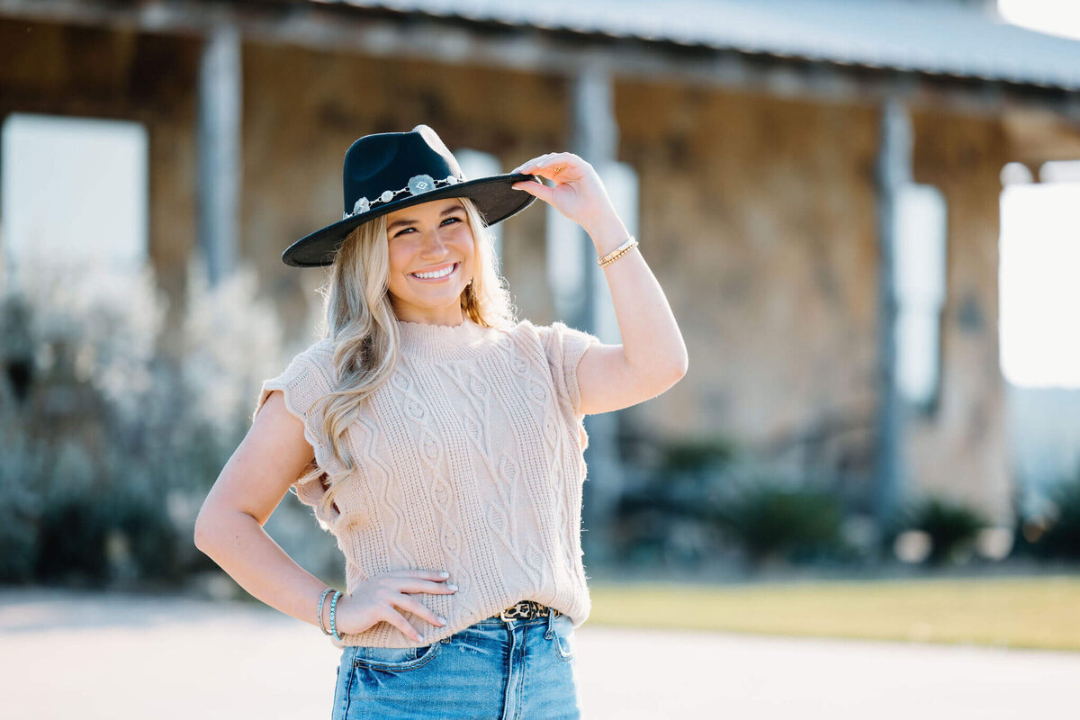 senior photo of Spring Hill senior standing in front of The el Cerrito Lodge wedding venue wearing light tan sweater, jeans, and black hat